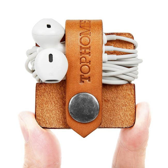 Hand holding the brown organizer with earbuds wrapped around it