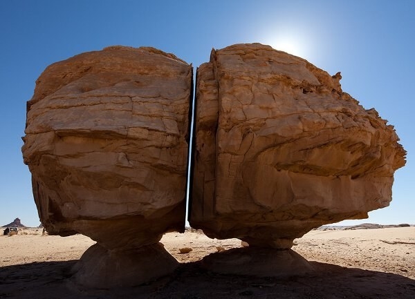 A very large rock formation that is split perfectly down the middle, in a straight line only a few inches wide