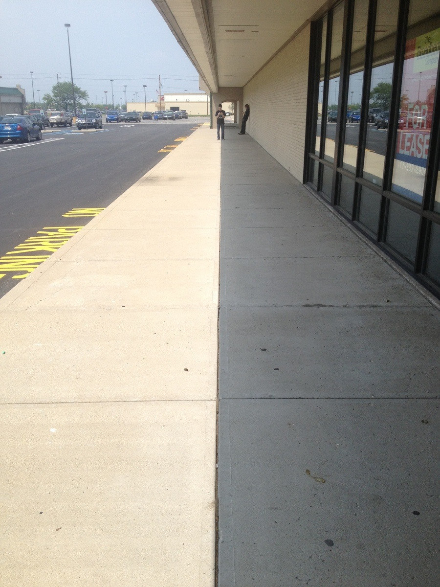 A sidewalk half-covered in shade, forming a perfect line down the middle that lines up with the sidewalk&#x27;s crack