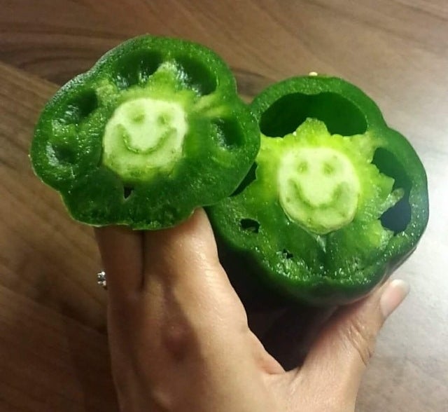 A green bell pepper that has been cut in half, but on the inside of the core there is a smiley face shape from the natural veining of the pepper