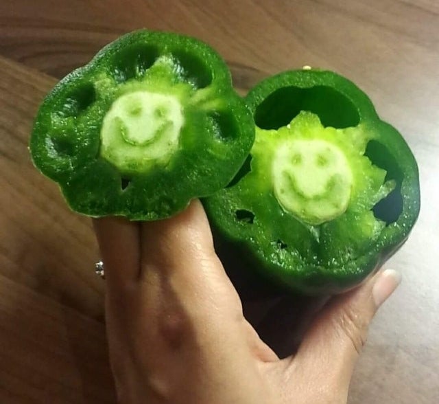 A green bell pepper that has been cut in half, but on the inside of the core there is a smiley face shape from the natural veining of the pepper