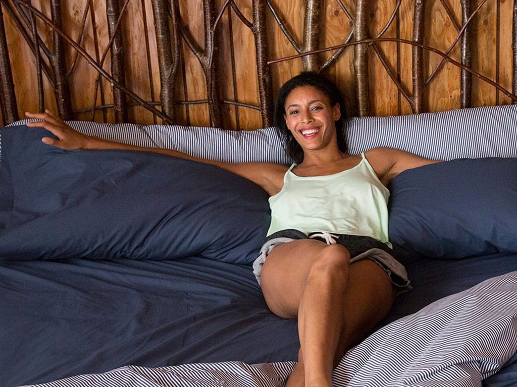A model lounging on a large bed with their arms over the king-sized pillows 