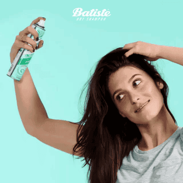 A gif of someone spraying the dry shampoo in their hair and rubbing