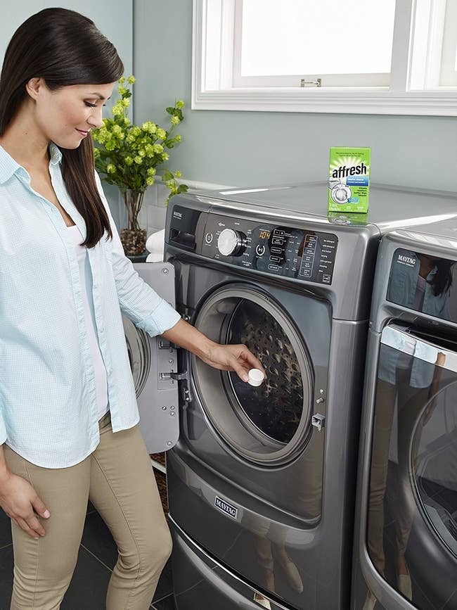 person putting a cleaning tablet into a front loading clothes washing machine