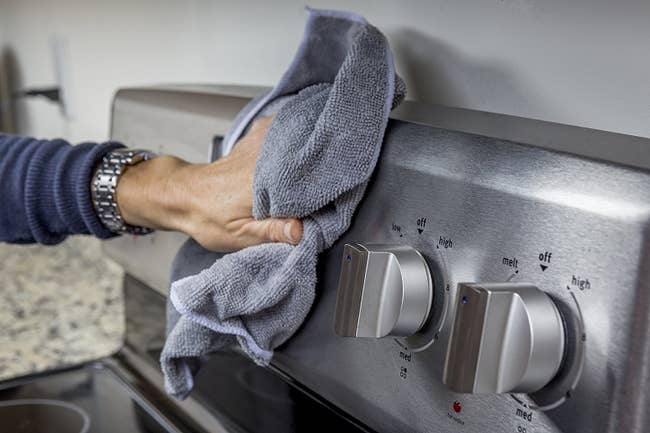person wiping a stainless steel oven with cleaner