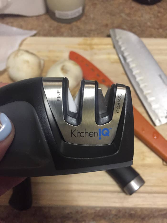 hand holding the knife sharpener over a cutting board with knives