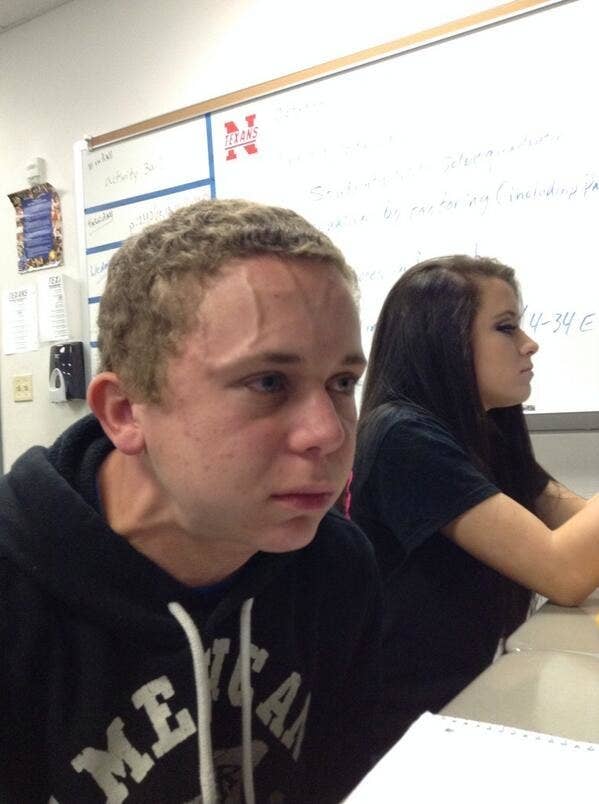 Teenage boy sitting in a classroom next to a girl with the veins in his forehead and neck bulging