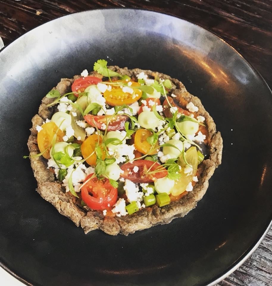The mouthwatering toasted masa cake is a popular street food in Oaxaca. The crispy, charred corn tortilla is topped with roasted asparagus, heirloom cherry tomatoes, queso fresco, and micro basil and smothered in black bean and arbol salsa.