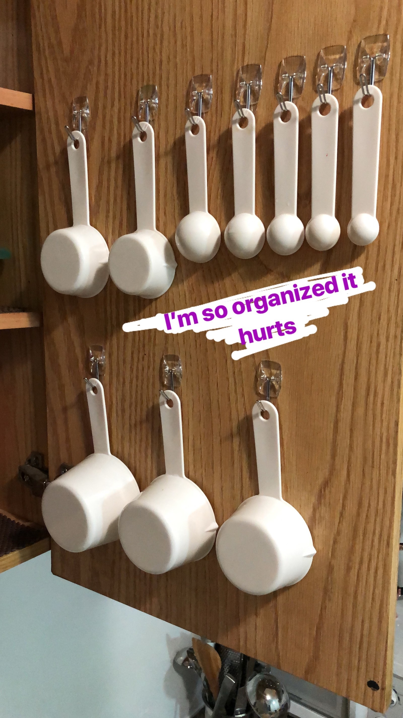 writer's pic of inside of a kitchen cabinet with mounted Command hooks to hanging measuring cups and spoons from 