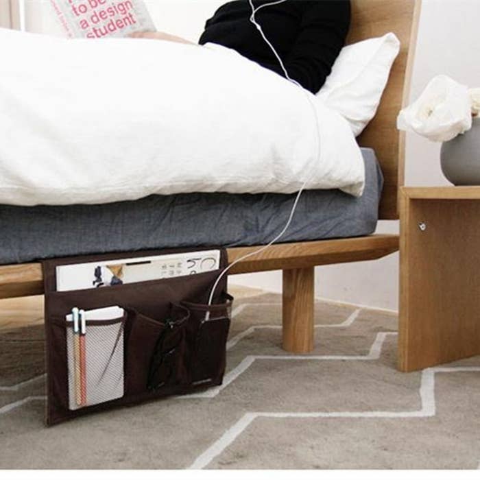 bed with caddy hanging off the bed frame and holding several items like a magazine, phone, glasses