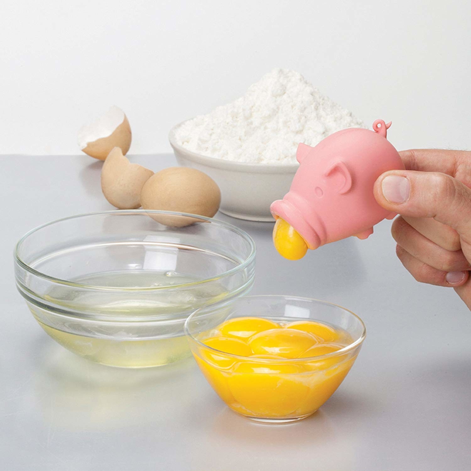 A pig-shaped silicone suction tool pulling up an egg yolk from a bowl