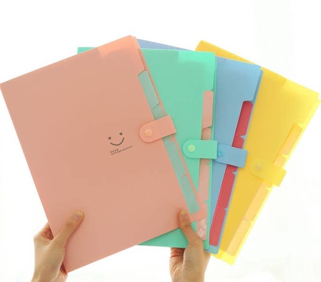Model holding up thin snap closed file folders in pink, green, blue, and yellow 