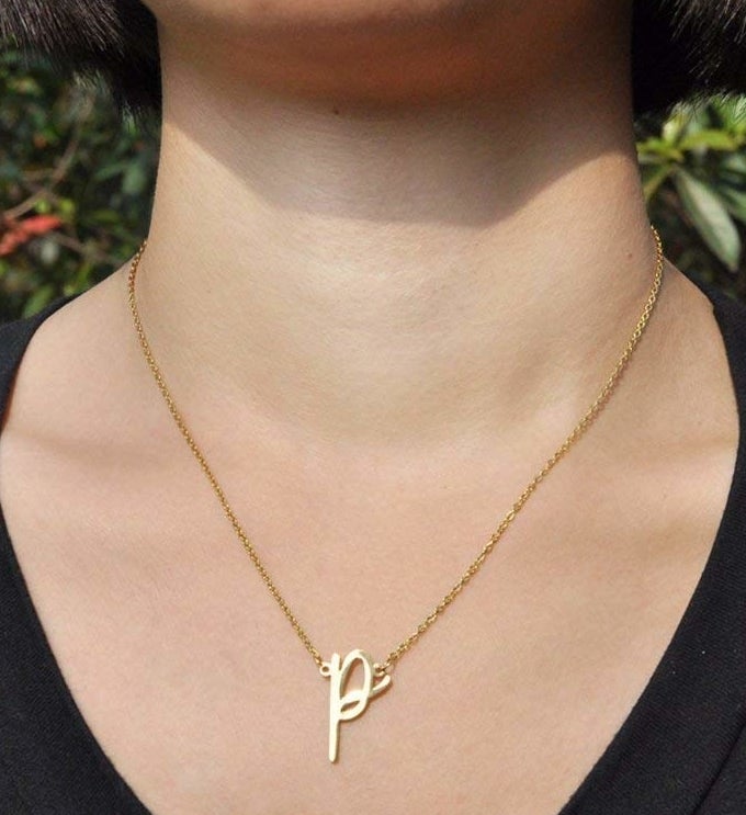 A model wearing the gold necklace with a letter &quot;P&quot; pendant