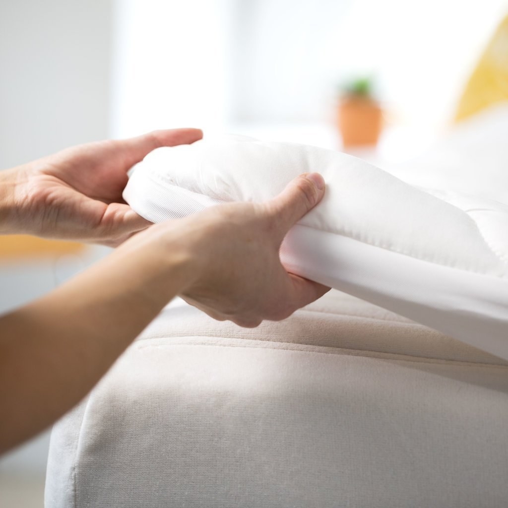 hands putting a fluffy mattress topper on a mattress