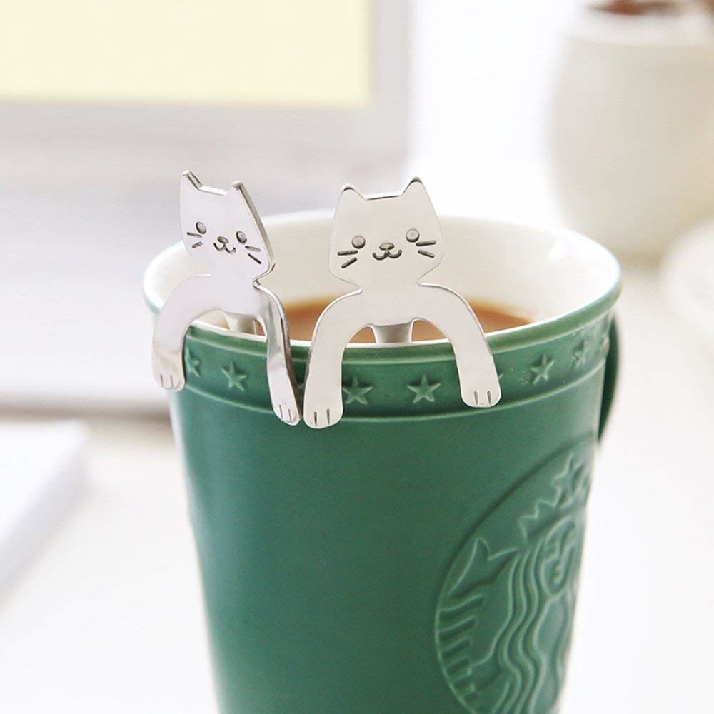 spoons with cats on the ends with arms that hook onto the side of the mug