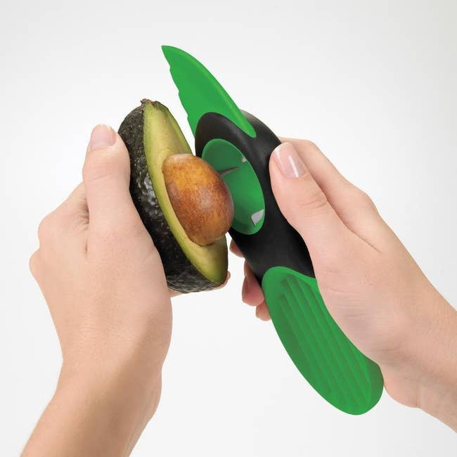 Hands using the three-in-one tool to pit an avocado