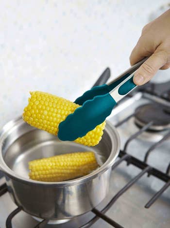 Hands using the tongs to pick up corn on the cob