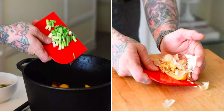 Person using red bench scraper to drop cut green onions into black pan and scoop up yellow onions