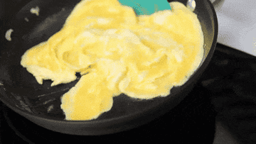 Plastic spatula stirring scrambled eggs around a nonstick pan