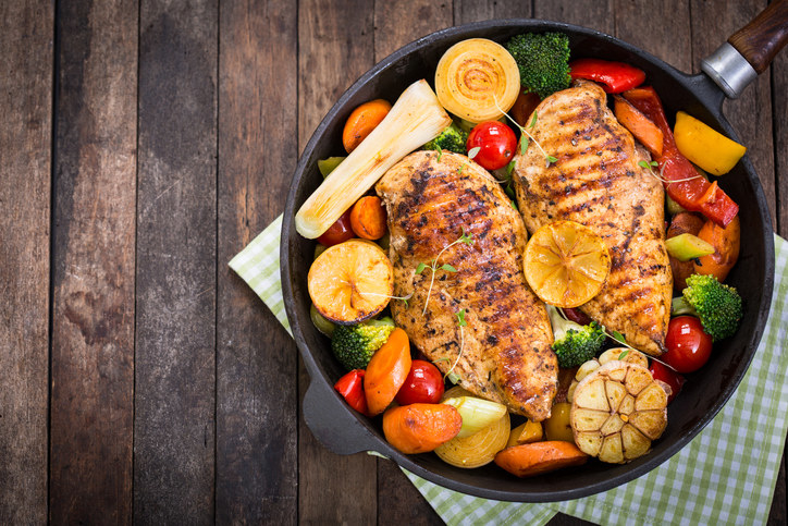 Metal pan filled with browned chicken and cooked vegetables, on a wooden surface