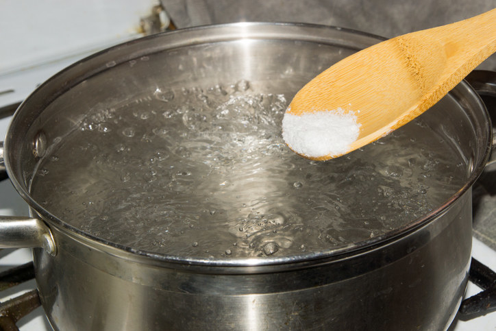 Wooden spoon with a tablespoon of salt being poured into a pot of boiling water