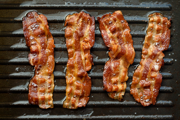 Greasy strips of bacon on griddle surface
