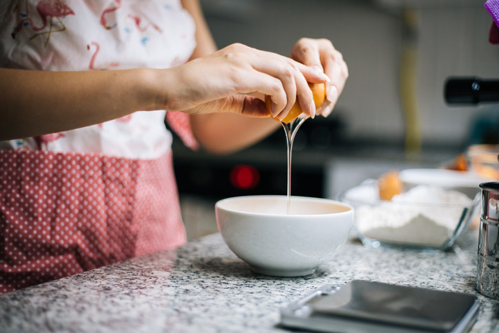 Woman cracking an egg into a small white bowl