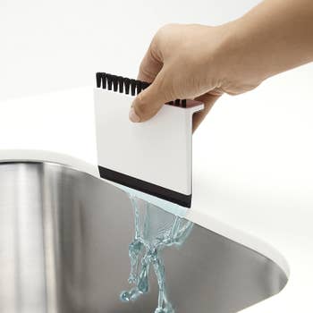 Hand using the squeegee side to sweep water into sink
