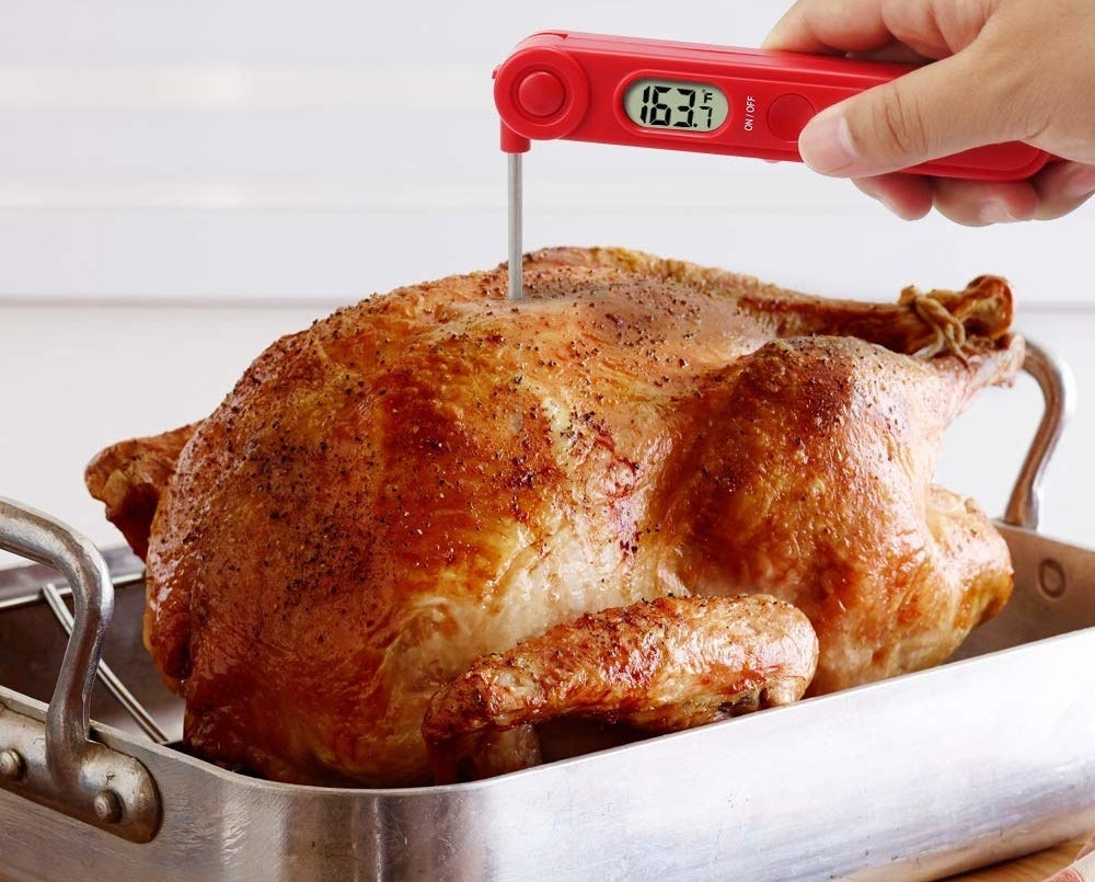 a digital meat thermometer being stuck into a freshly roasted chicken