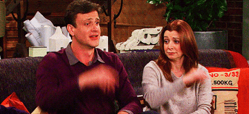Jason Segel and Alyson Hannigan sitting on a couch and snapping their fingers