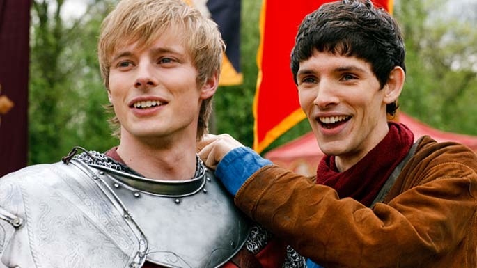 Bradley James and Colin Morgan smiling at something in front of them