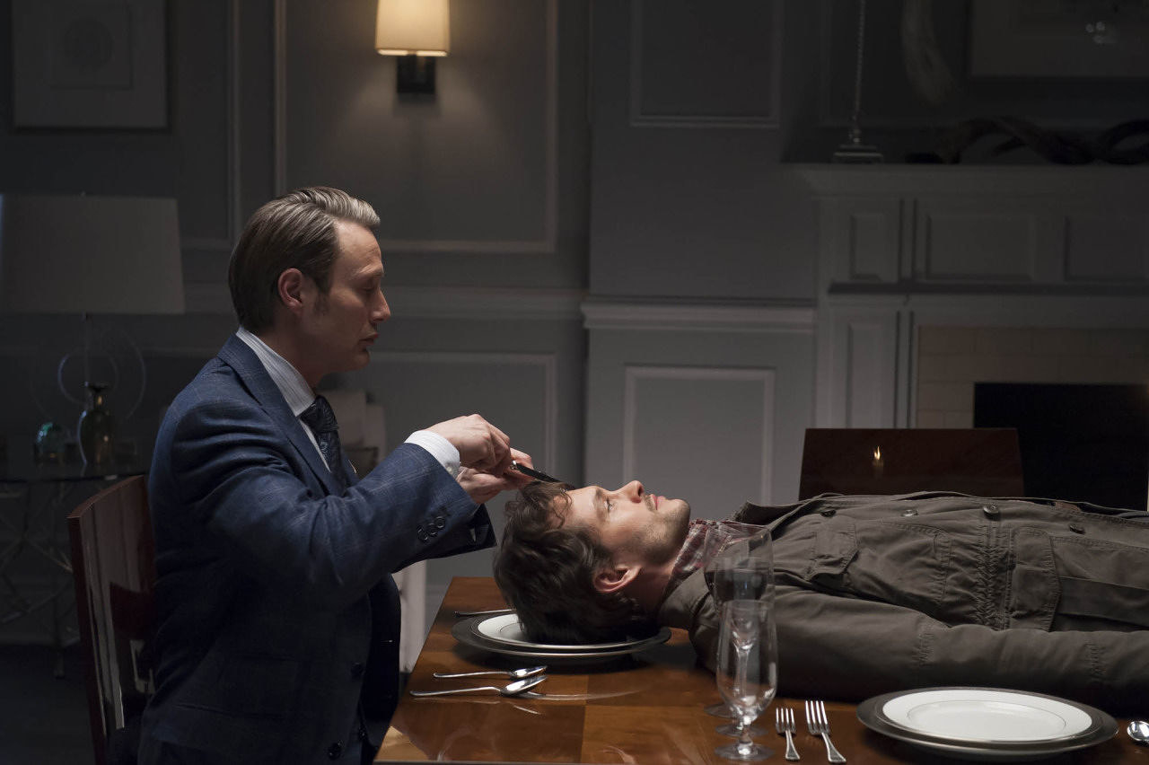 Mads Mikkelsen as Hannibal appearing to carve the head of Hugh Dancy as Will Graham, who&#x27;s lying on a dining table
