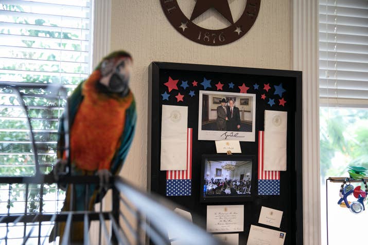 A framed photograph of Anwar Khalifa with former President George W. Bush shares space with Kiwi, Khalifa&#x27;s pet macaw, in his office.