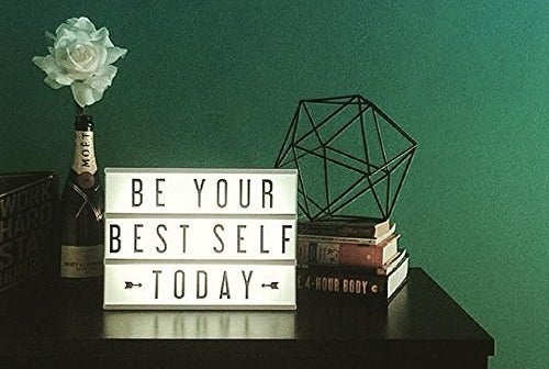 A Cinema Lightbox that says &quot;Be Your Best Self Today&quot; on a table next to some books and a flower