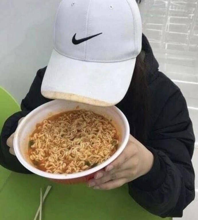 Person with a white cap raises a bowl of noodle soup to their face