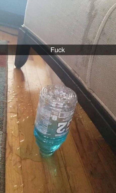 An overturned bottle with liquid in it and no top rests on a wood floor