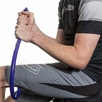 A model using the massager to target a spot on their hamstring; they hold it by a handle at the bottom of the question mark shape