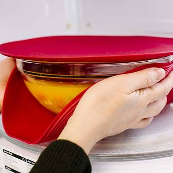 Two hands grabbing either side of the bowl with the large cover; the bowl is covered with the small cover