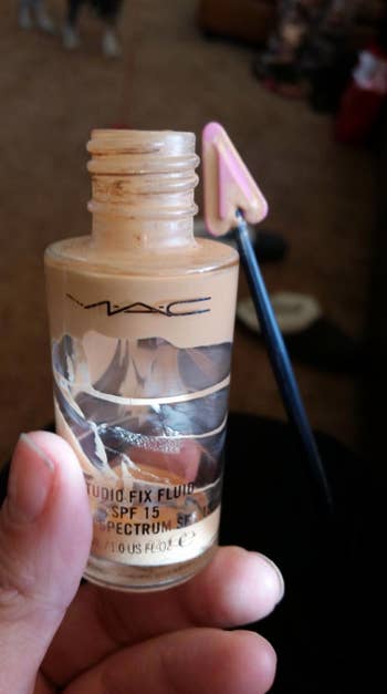 reviewer using thin pointed stick to get concealer out of a jar 