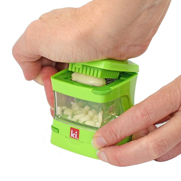 a hand using the press to shop garlic