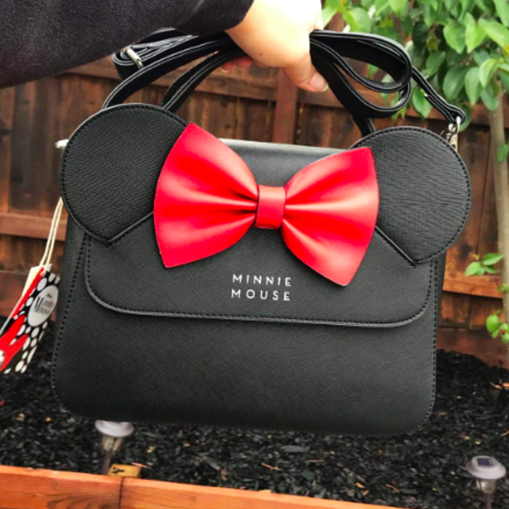 A reviewer holding the bag by the top handle. The top flap with the ears and bow reads "Minnie Mouse"