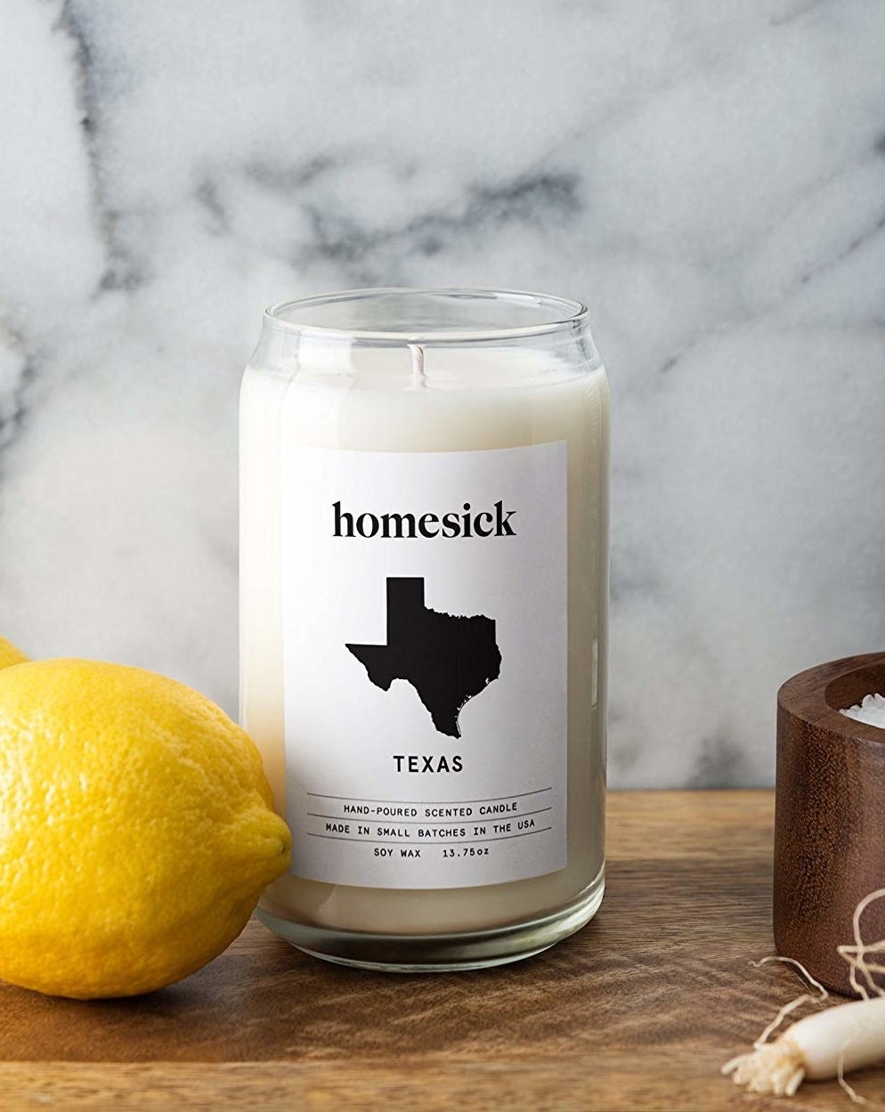 The candle with white wax in a clear cup with a white label that says &quot;Homesick&quot; and Texas with an image of the state