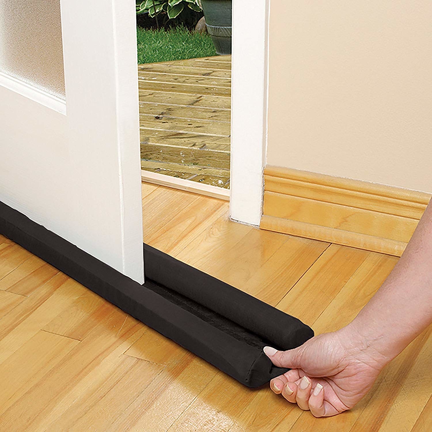 A hand pushing the guard under the door; it has two long foam cylinders that sit on either side of the door, and fabric beneath that joins them 