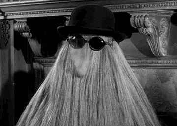 gif of cousin itt from the adams family wearing sunglasses and exhaline smoke through its curtain of hair