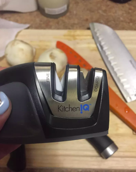 hand holding the kitchen sharpener in front of a cutting board with knives
