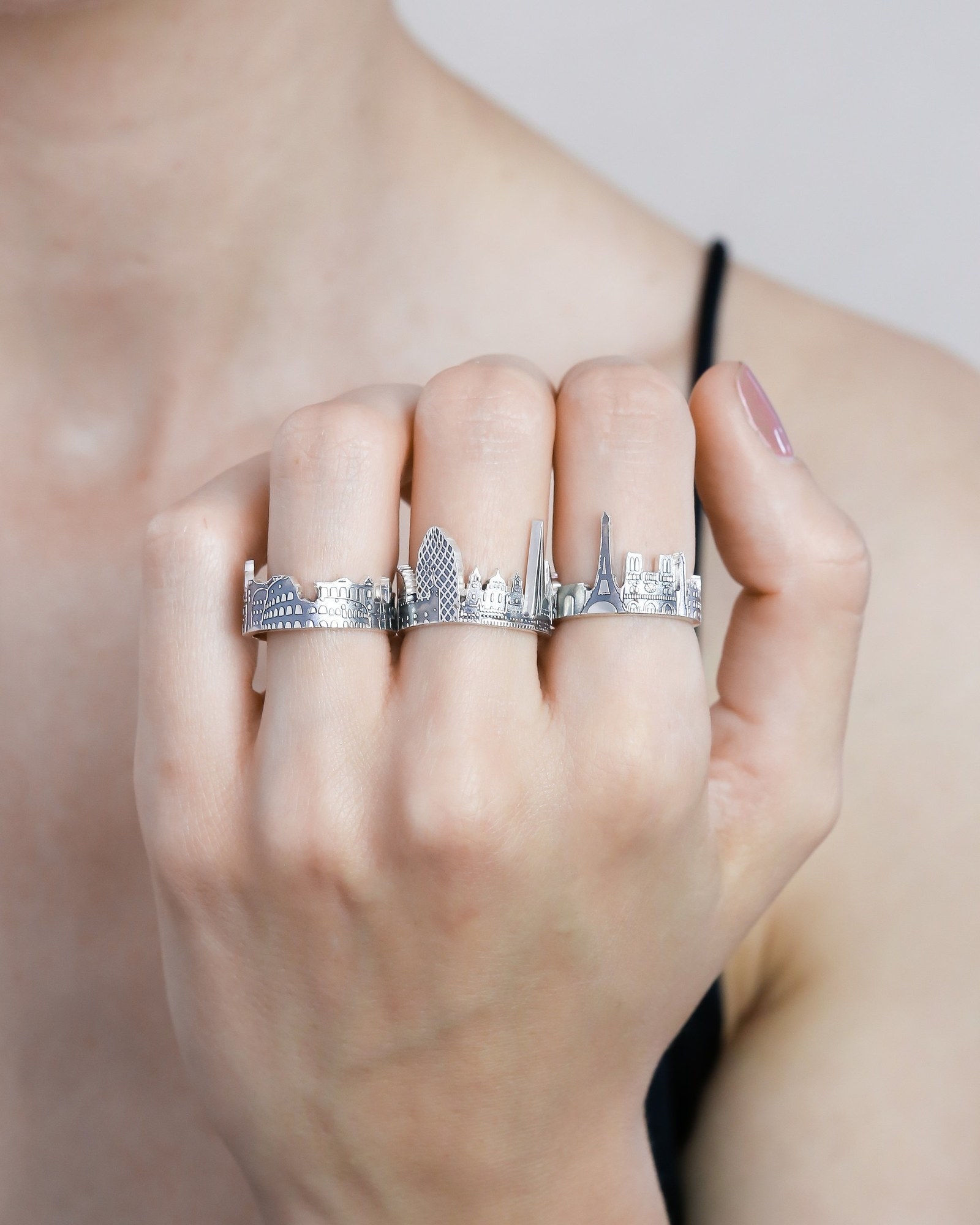 A hand with silver rings with Paris, London, and Rome skylines