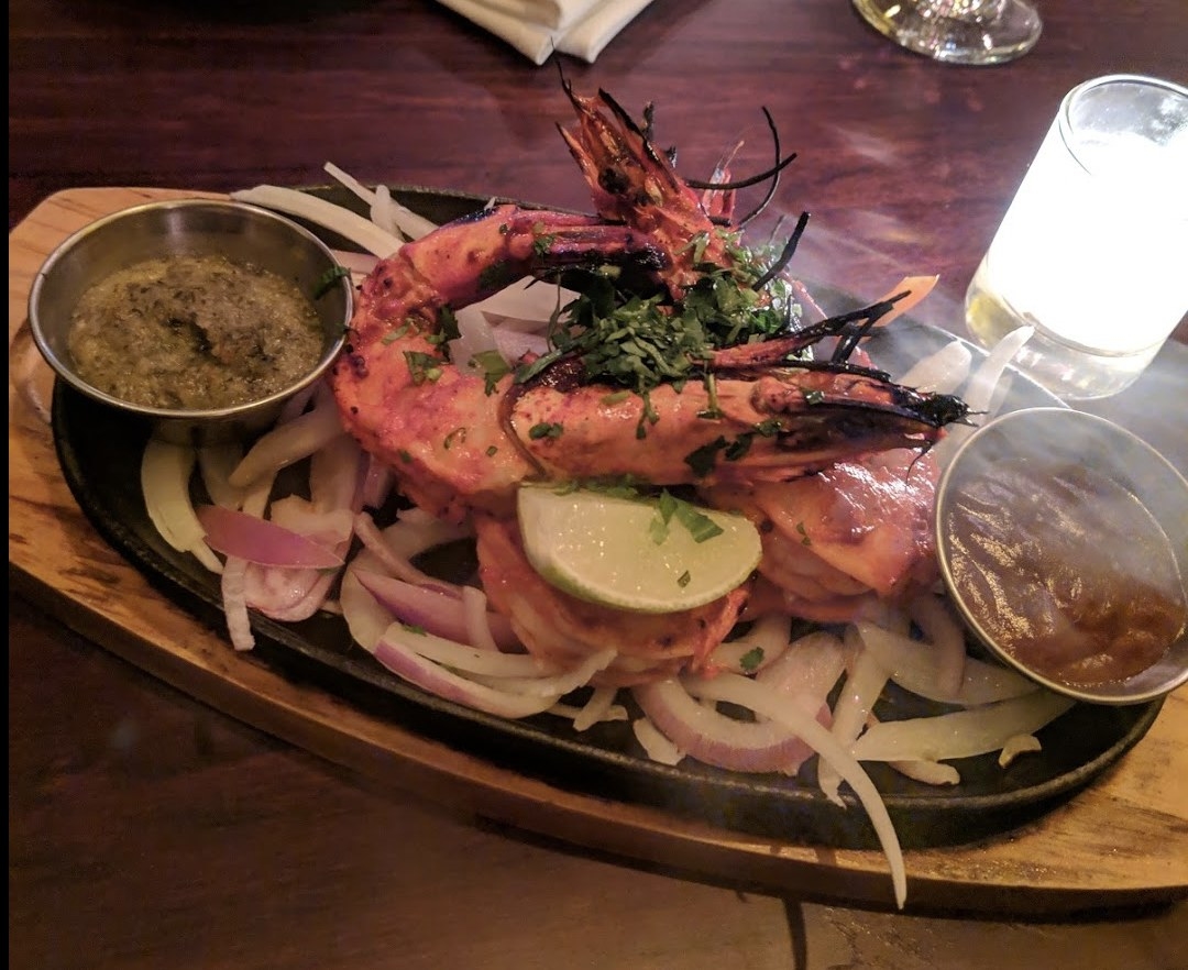 Served sizzling on the grill, these three large tiger prawns are seasoned in classic five-spice marinade and served with mint chutney and barbecue sauce over a bed of onions and bell peppers.