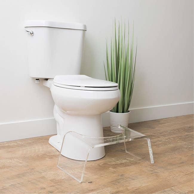 The clear step stool with a rounded side against a toilet