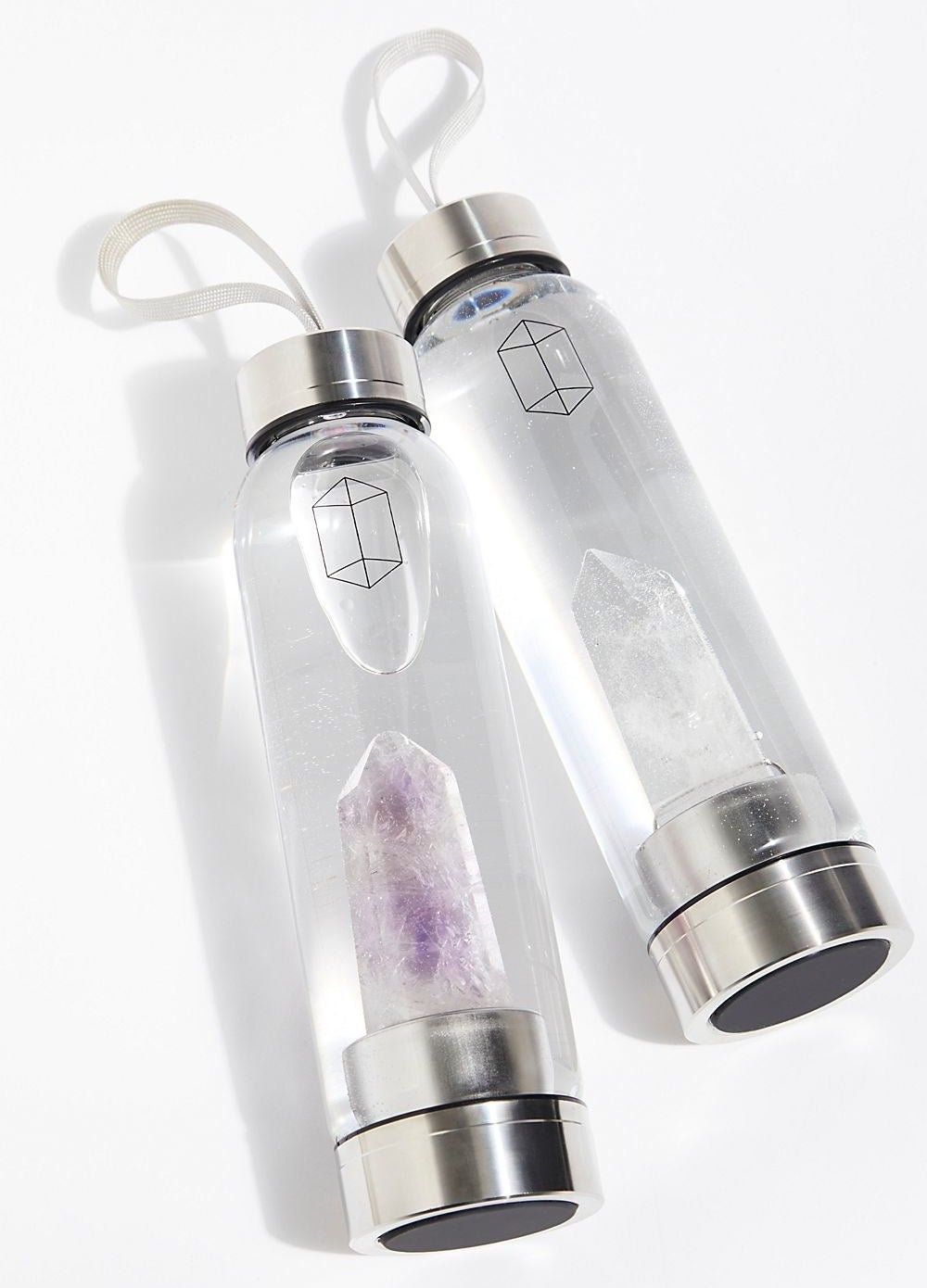 Two clear water bottles with silver bottoms and caps and crystals in the bottom of them