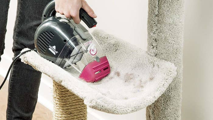 hand using a hand vac on a fur-covered cat tree